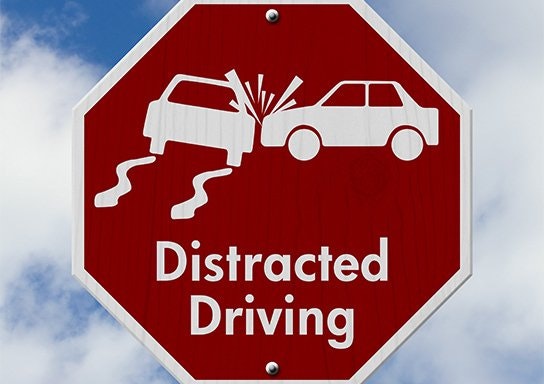 A red stop-sign-shaped sign with symbols indicating a car crash and the words "Distracted Driving."