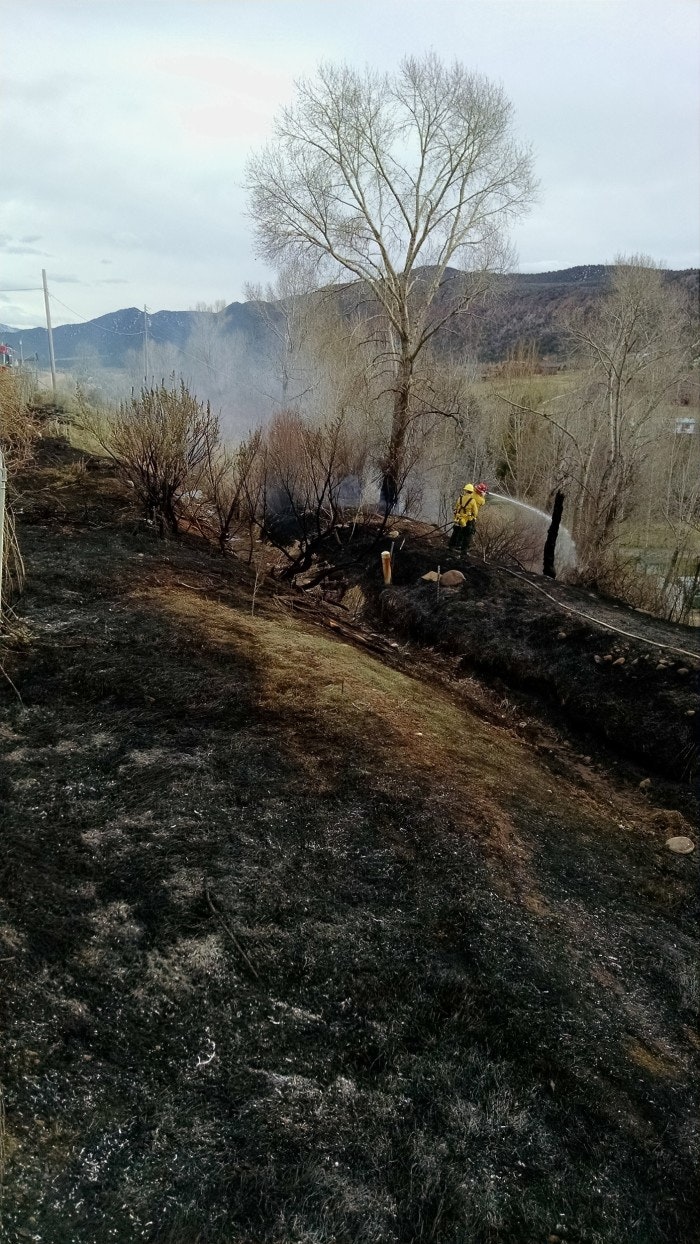 A firefighter is extinguishing a small ground fire amidst charred landscape.