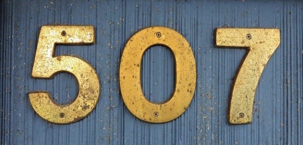 Rusty golden numbers "507" on a blue background.
