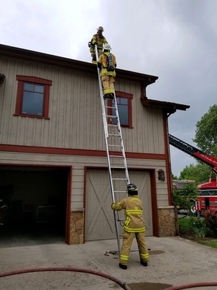 Firefighters training with ladder against two-story building.