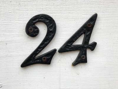 Metal house numbers "24" mounted on a white wall.