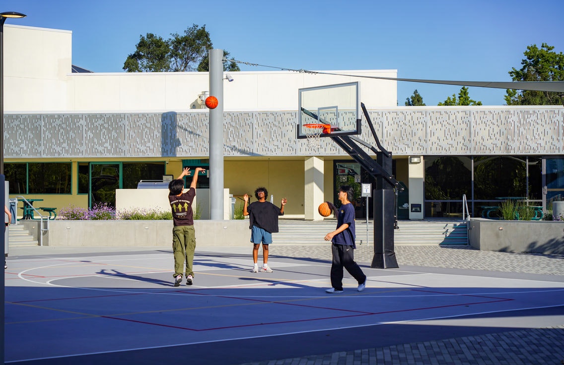 Three people playing basketball outside near a building.