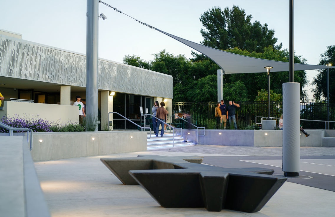 An outdoor modern space with people, concrete seating, trees, and a building with illuminated steps.