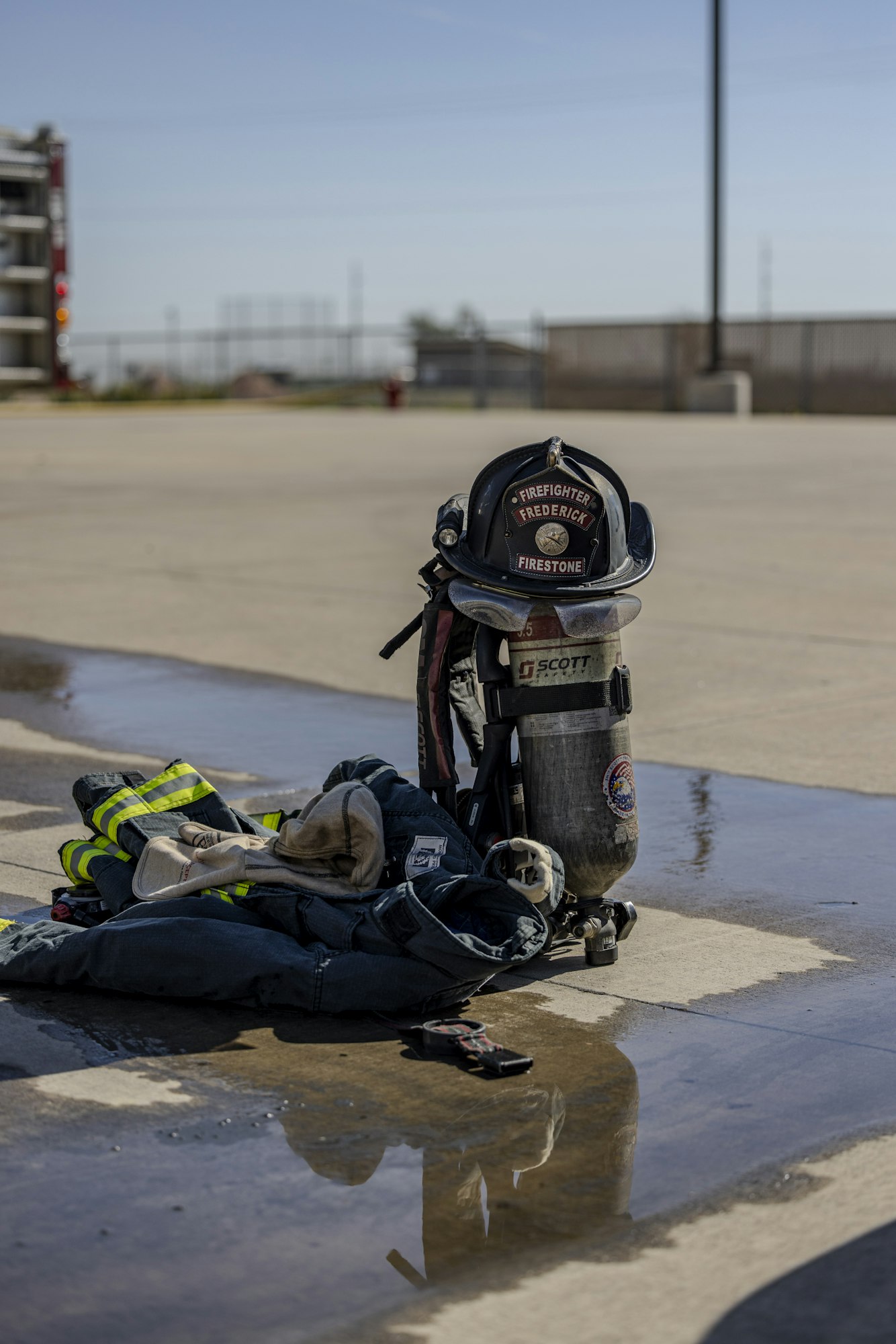 The image shows a firefighter's gear, including a helmet, breathing apparatus, and clothing, laid out on a wet surface.