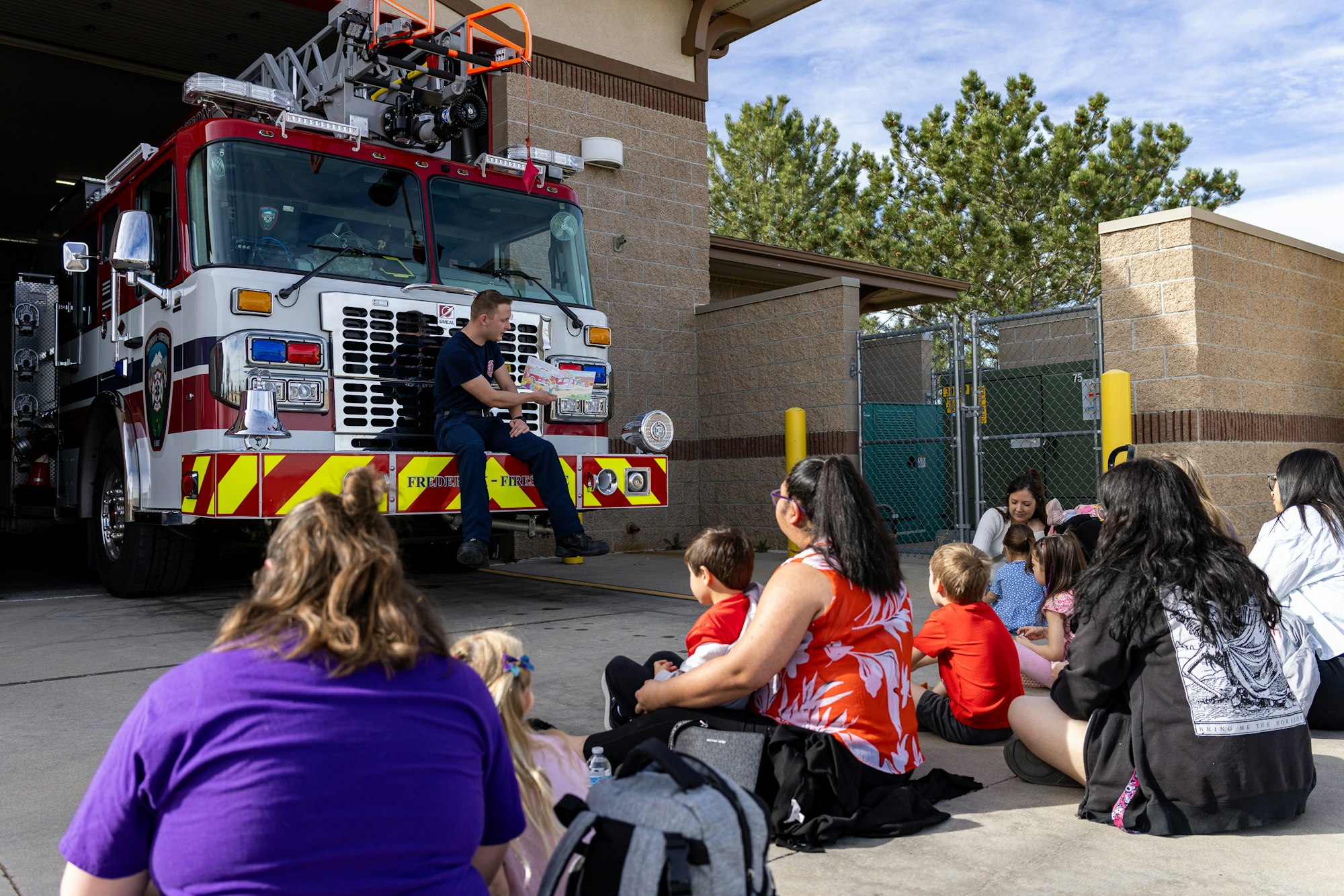 A firefighter engages a group of children and adults in front of a fire truck during an educational event.