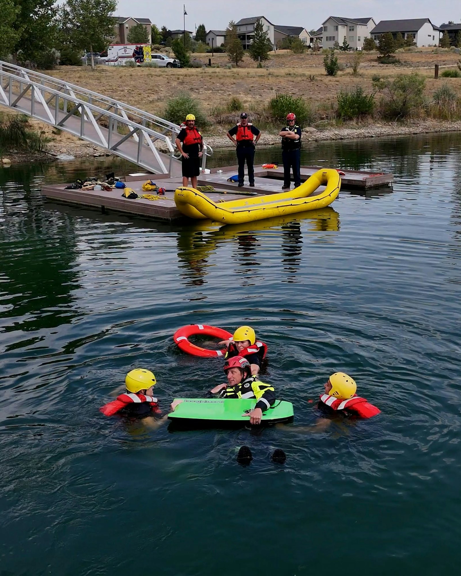 Rescue personnel practice water safety, with some in the water using floats and others on a dock observing the drill.