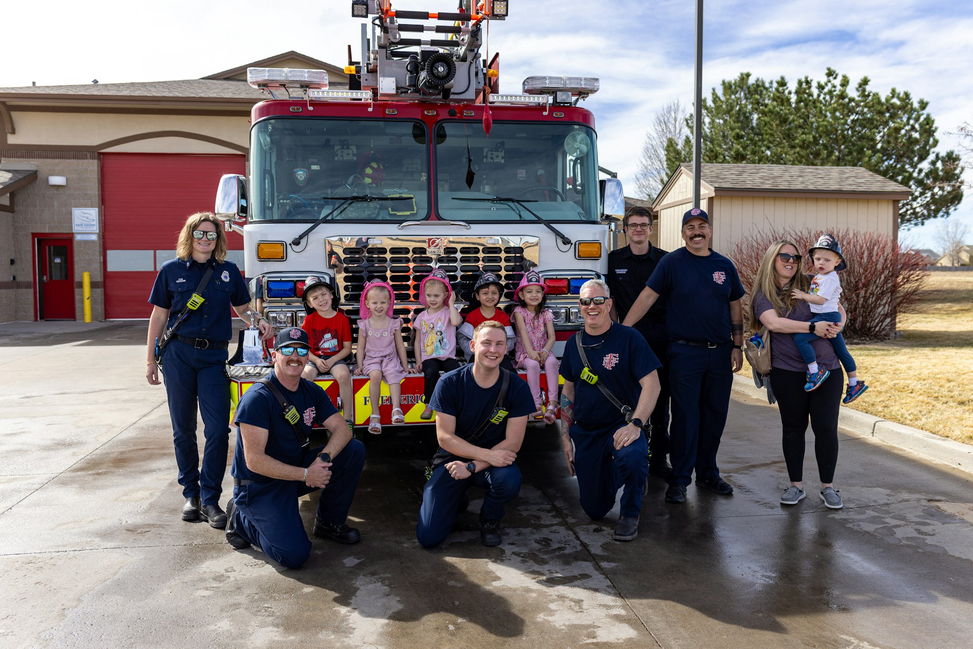 A group of firefighters poses with children in front of a fire truck, promoting community engagement and safety awareness.