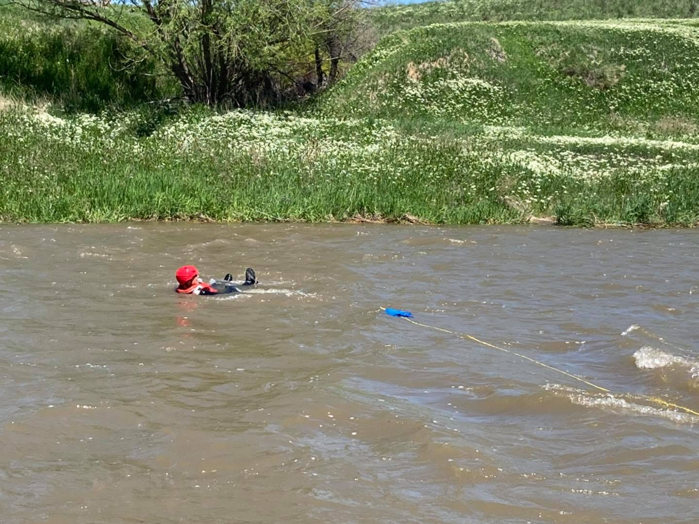 A person in red helmet and life vest floating in a river, attached to a blue rope.
