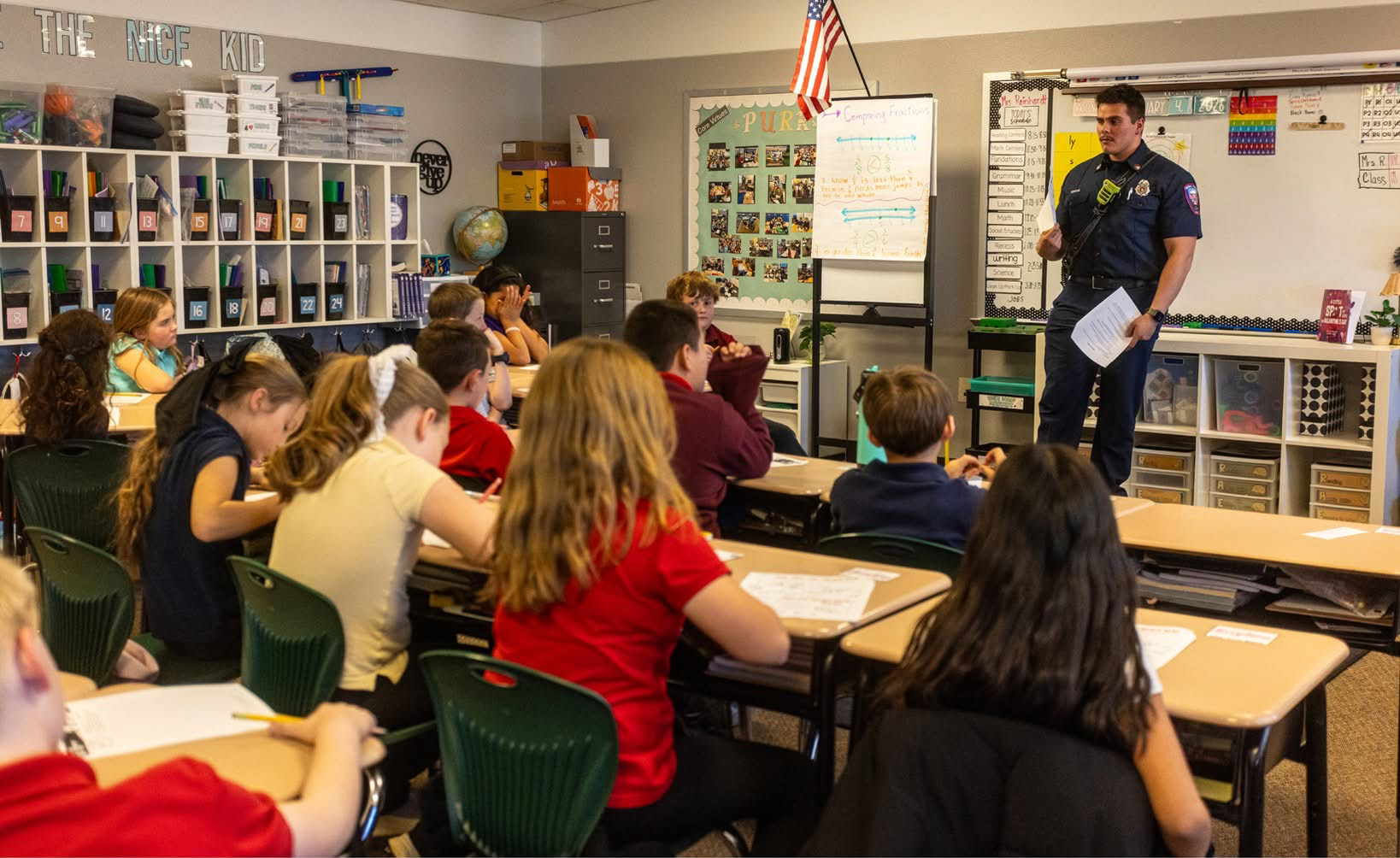 A classroom of students listens to a police officer giving a presentation, with focus on safety and community awareness.