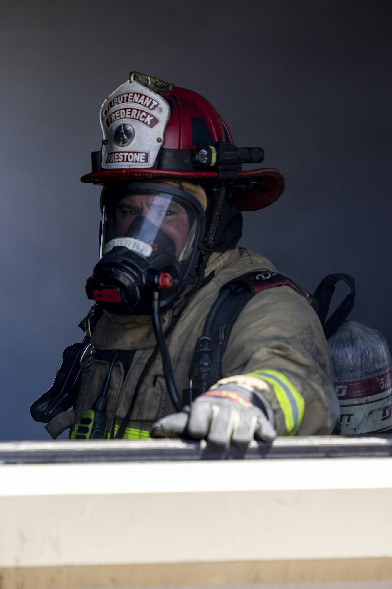 A firefighter in gear, including a helmet and mask, is preparing to respond to an emergency situation.