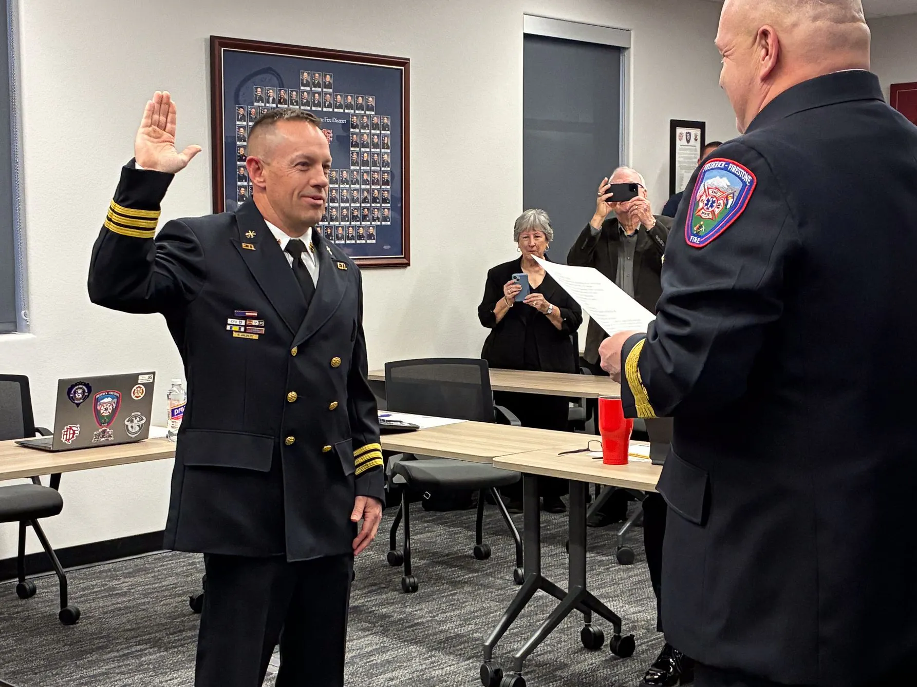 A man in uniform is being sworn in, raising his hand as a few onlookers observe in a formal setting.