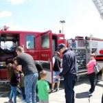 People exploring a fire truck with a firefighter present, possibly at a community event or demonstration.