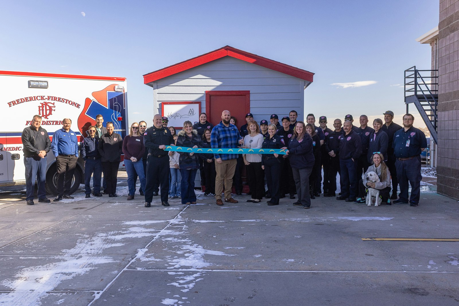 A large group of people, including firefighters and officials, poses for a ribbon-cutting event outside a building.