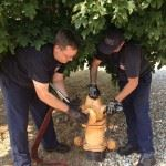 Two firefighters helping a child in firefighter gear hold a hose.