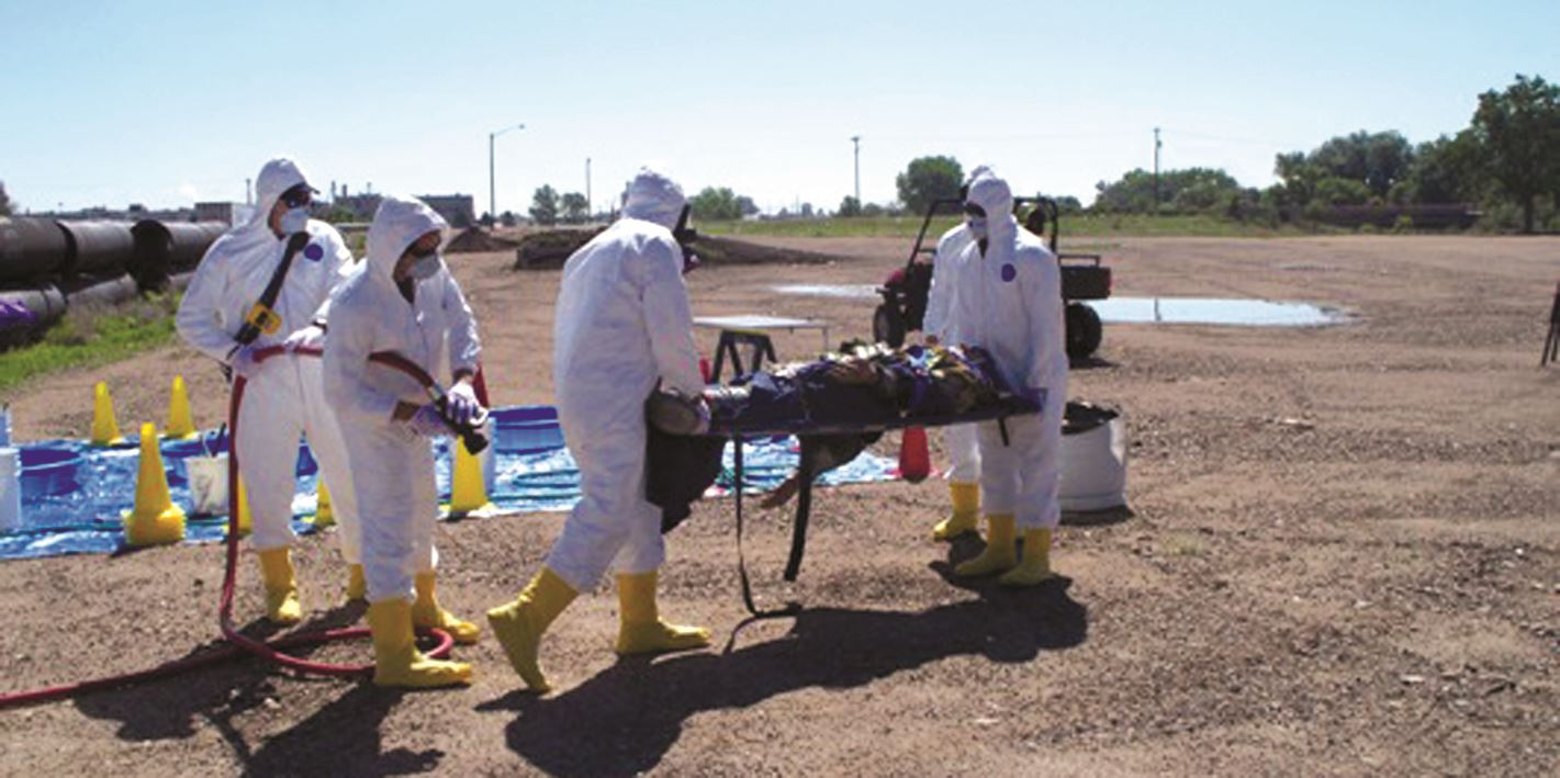 People in hazmat suits conducting an outdoor exercise or responding to an incident with a stretcher.
