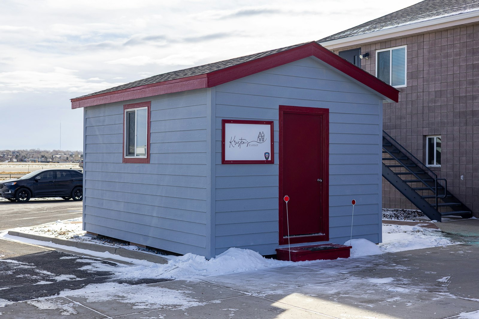 A small blue building with a red door and trim, featuring a sign labeled "Kirsten's Closet," surrounded by snow.