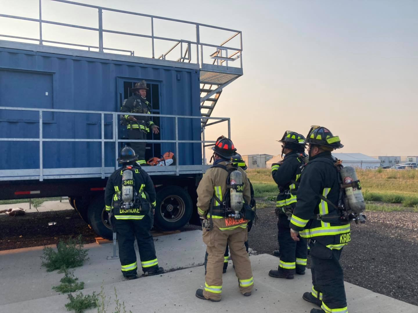 Firefighters gathered around a training structure, possibly discussing strategy or receiving instructions.