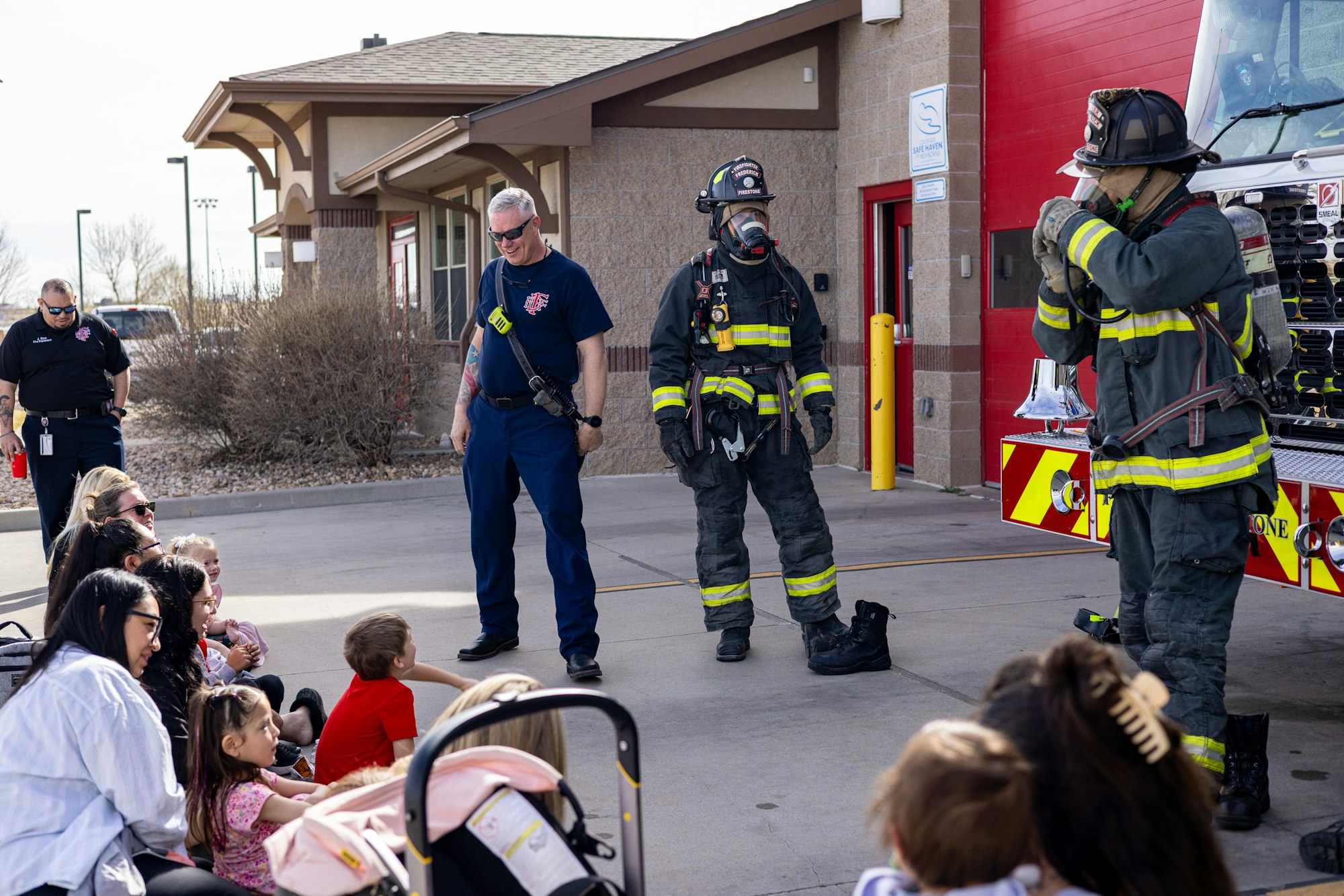 Firefighters interact with children and families during a community event outside a fire station. Education and engagement are key themes.