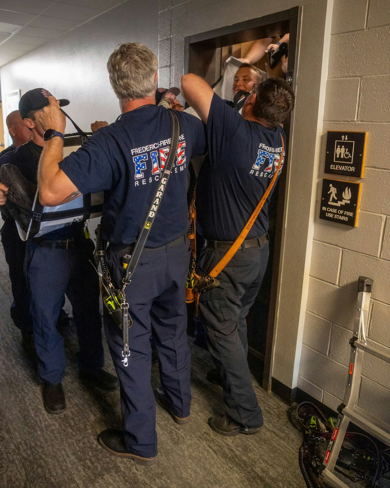 Firefighters are responding to a situation, with several assisting a person near a door in a hallway.