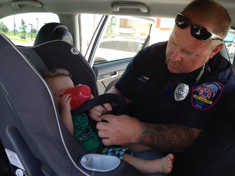 A firefighter checking a child's car seat while the child drinks from a sippy cup.