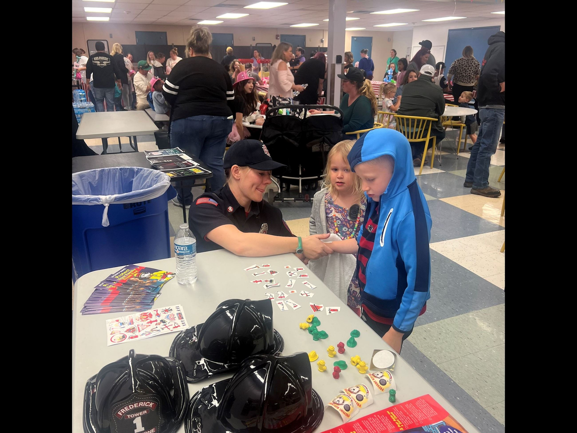 A community event with a firefighter interacting with children, tables with activities, and people in the background.