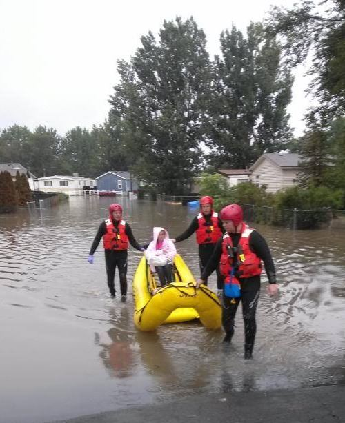 Rescuers in life vests with a raft assisting in a flooded residential area.