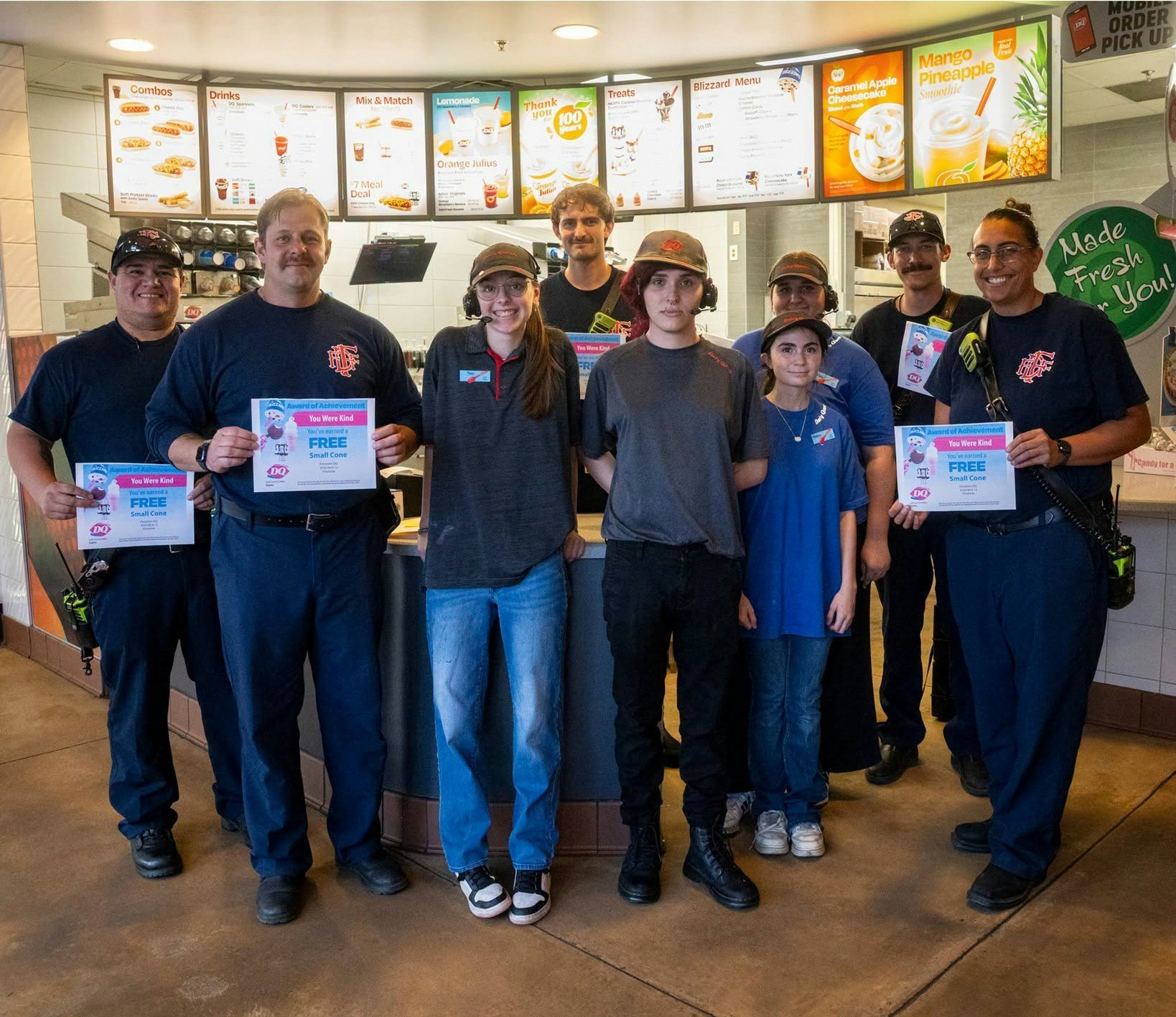 A group of firefighters and Dairy Queen staff hold certificates for free cones, celebrating kindness at the restaurant.
