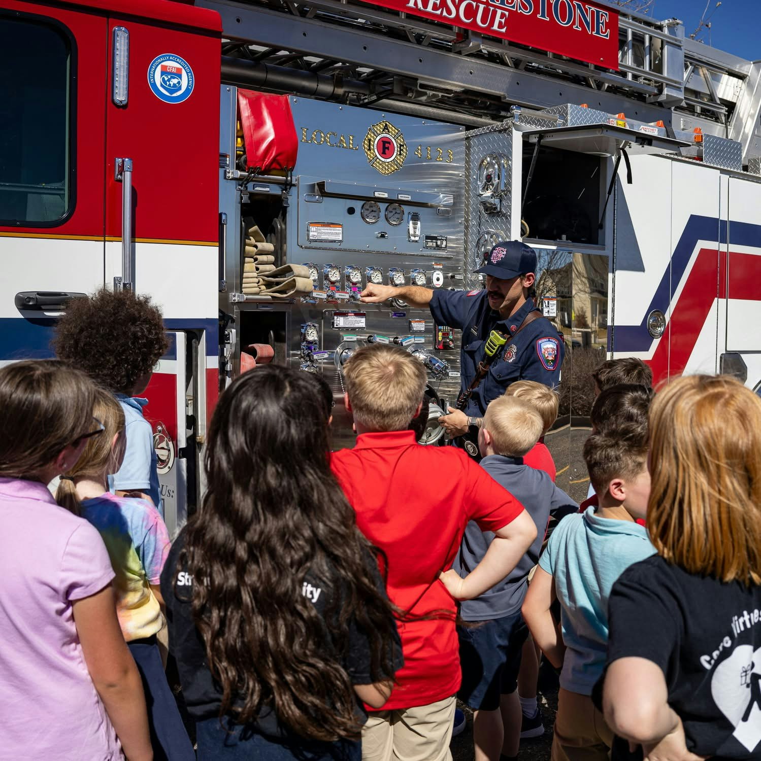A firefighter teaches a group of children about a fire truck and its equipment during a school visit.