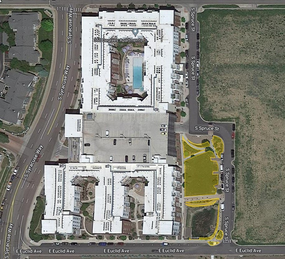 Aerial view of an apartment complex with a central pool, surrounded by roads and a vacant lot.