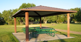 A park shelter with a roof and picnic tables on a sunny day.