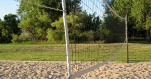 A sandy volleyball court with a net, trees in the background.
