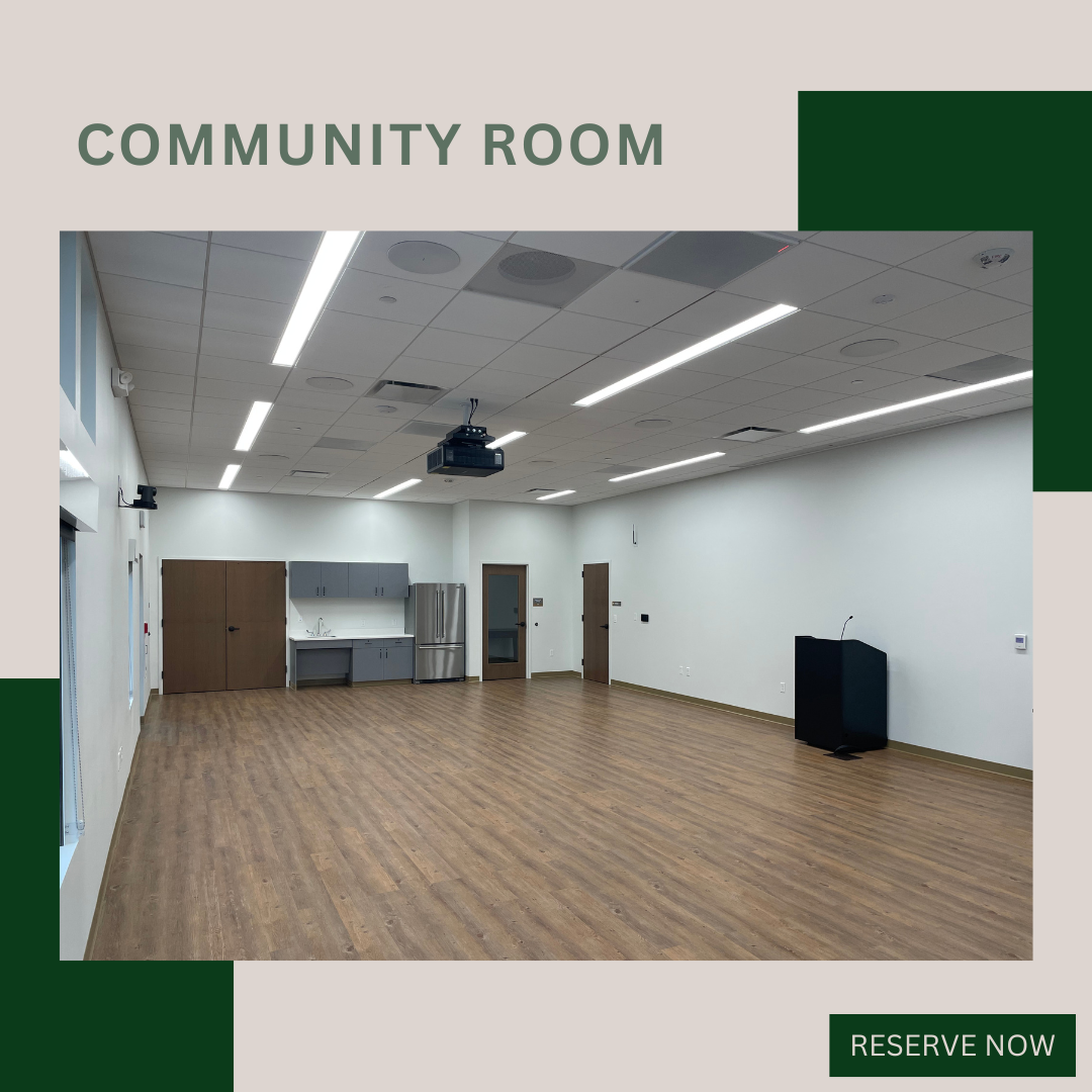 Empty community room with wood floor, ceiling lights, projector, podium, sink, and fridge. Text: "COMMUNITY ROOM. RESERVE NOW."