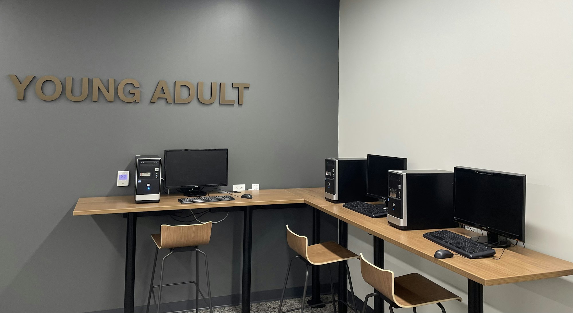 A room labeled "Young Adult" with desktop computers on wooden desks and chairs.