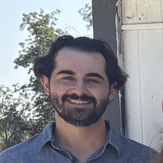 A smiling man with a beard, wearing a blue shirt, standing outdoors.