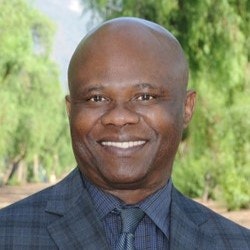 A person smiling in an outdoor setting with trees in the background.