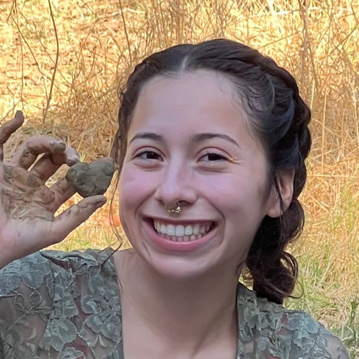 A smiling person with a nose ring, holding a dirty hand out with a small object.