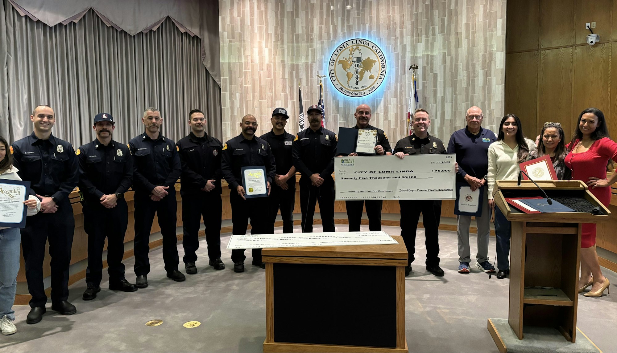 A group of people, including firefighters, holding a ceremonial check for $75,000 at a city event in Loma Linda, California.