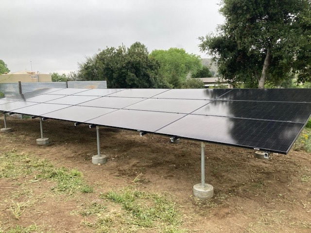 Solar panels installed on a ground-mounted structure surrounded by grass and trees.
