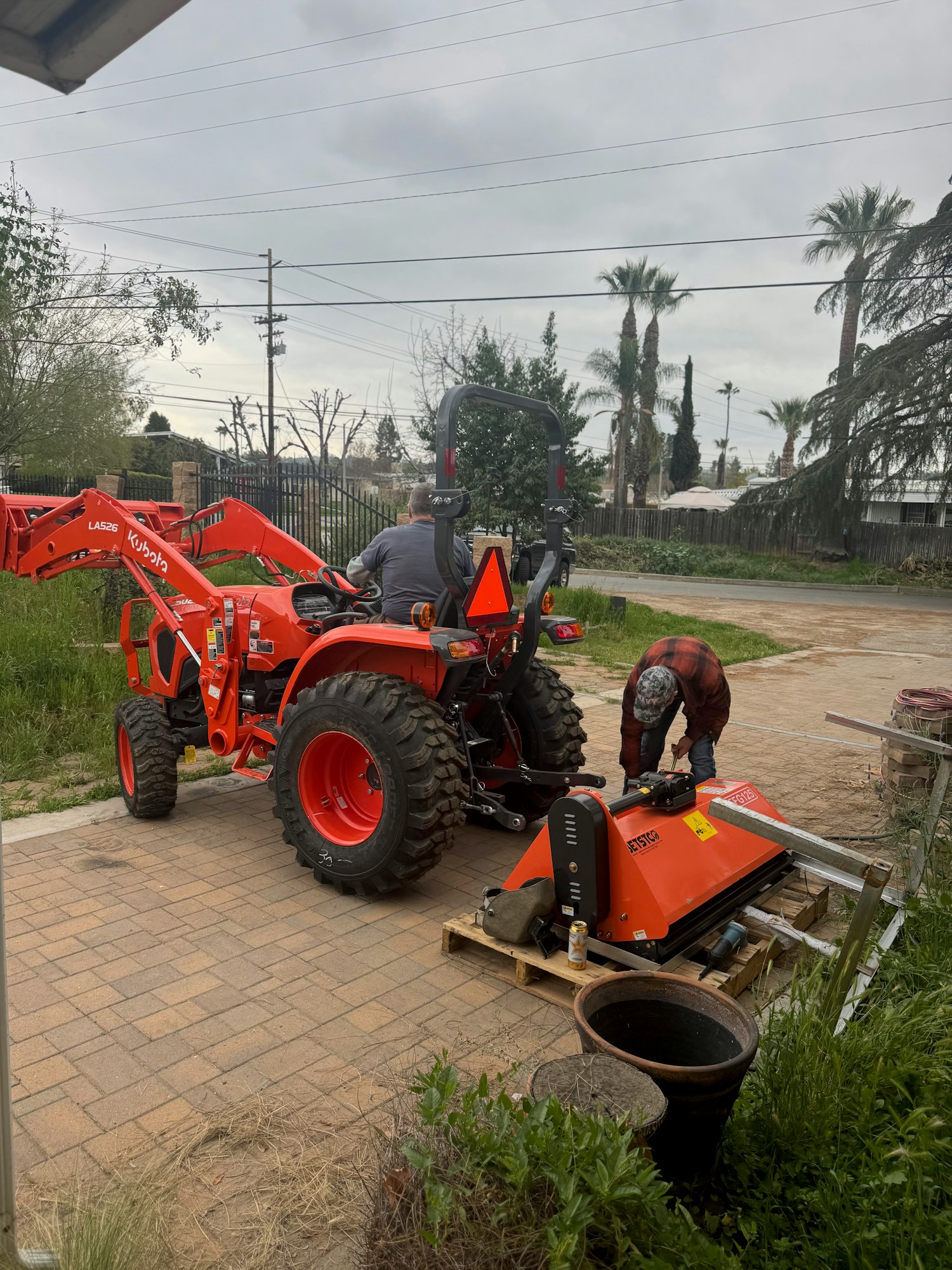 Two people work on a tractor near a pallet with equipment outdoors.