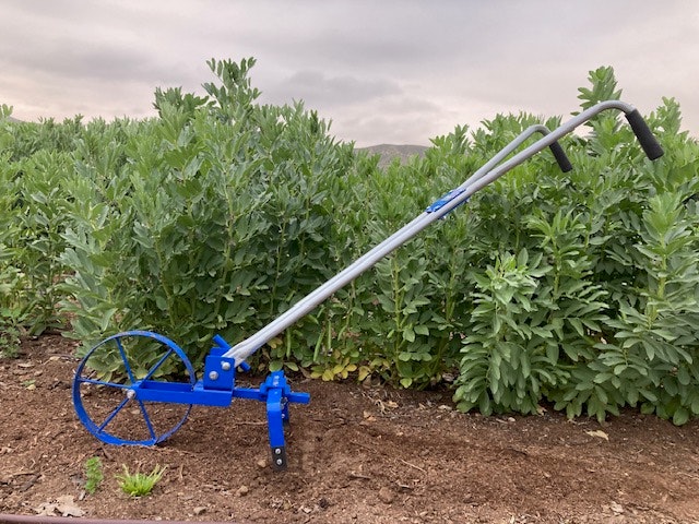 A garden tool with a blue wheel and handle for weeding, set in a field with green plants.