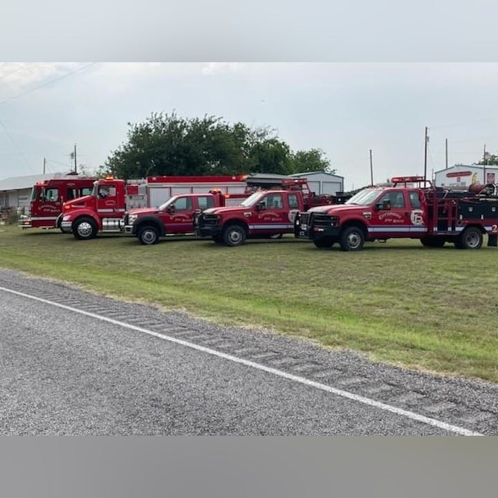 Four fire trucks parked on a grassy area near a road.