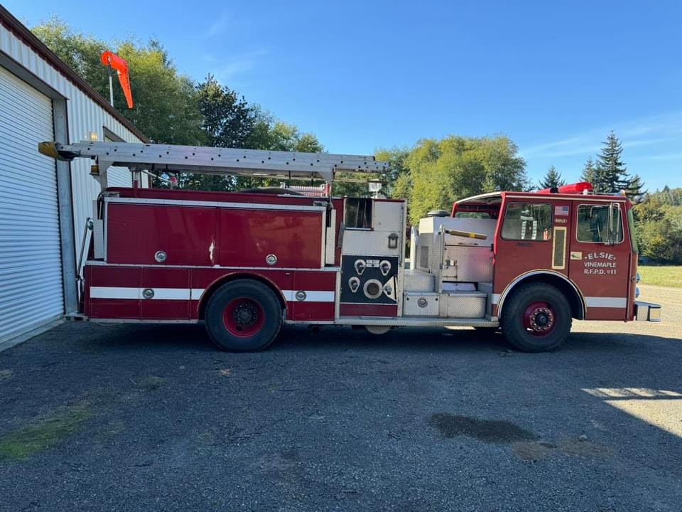 A red fire truck parked outside, with a ladder on top and clear blue skies above.