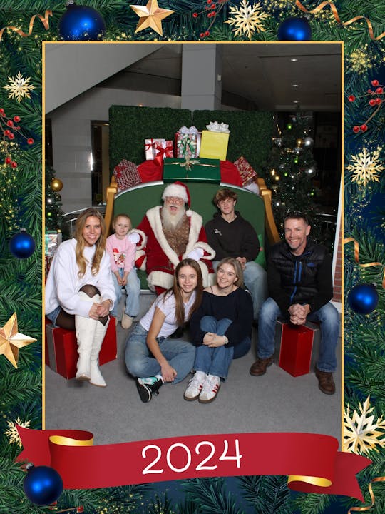 A group with Santa poses for a festive photo, surrounded by Christmas decorations with "2024" written at the bottom.