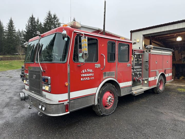 Red fire truck parked outside a garage on a cloudy day.