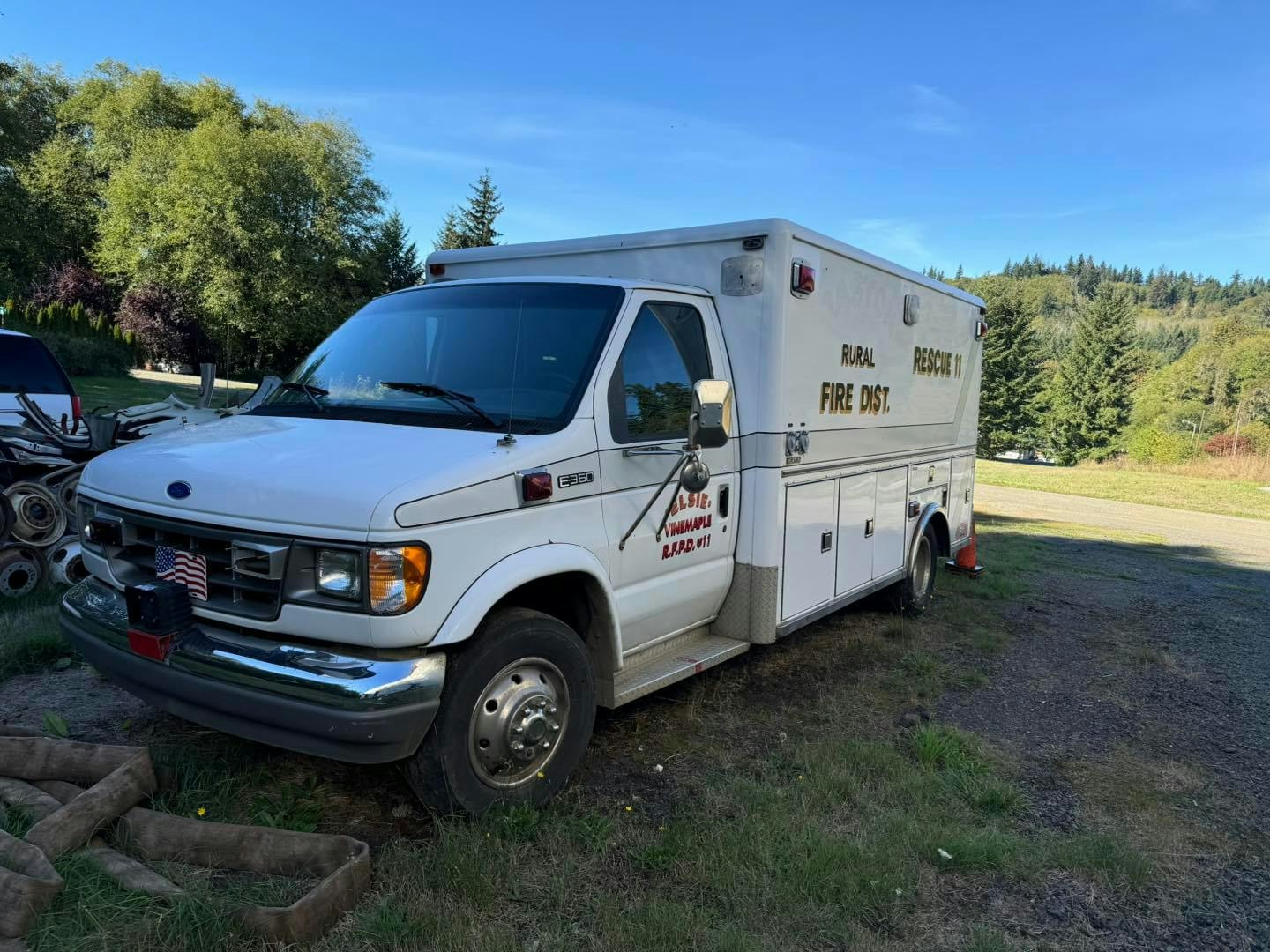 A parked ambulance from the Rural Fire District against a backdrop of trees and blue sky.