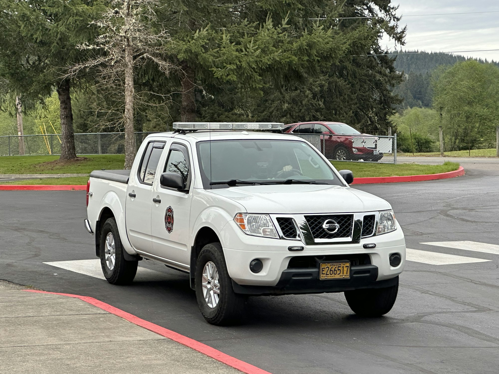 A white Nissan pickup truck marked with an emergency services emblem parked on a road with trees in the background.