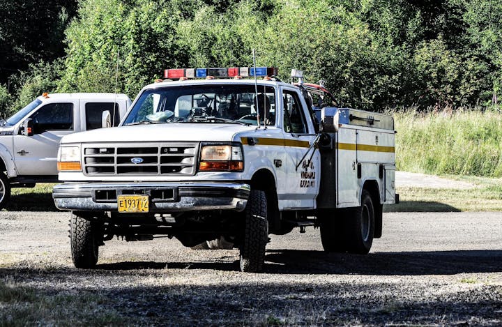 A white and yellow utility truck with emergency lights, parked on a grassy roadside.