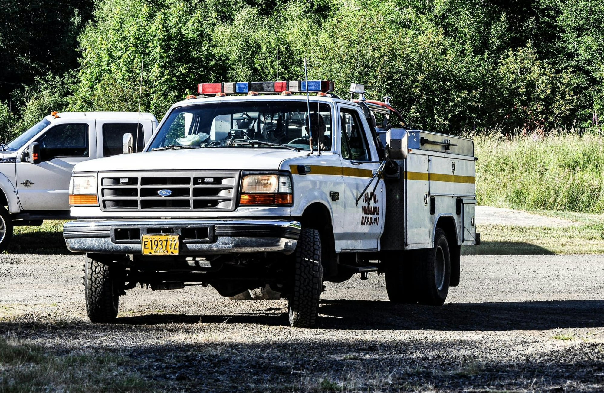 A white and yellow utility truck with emergency lights, parked on a grassy roadside.