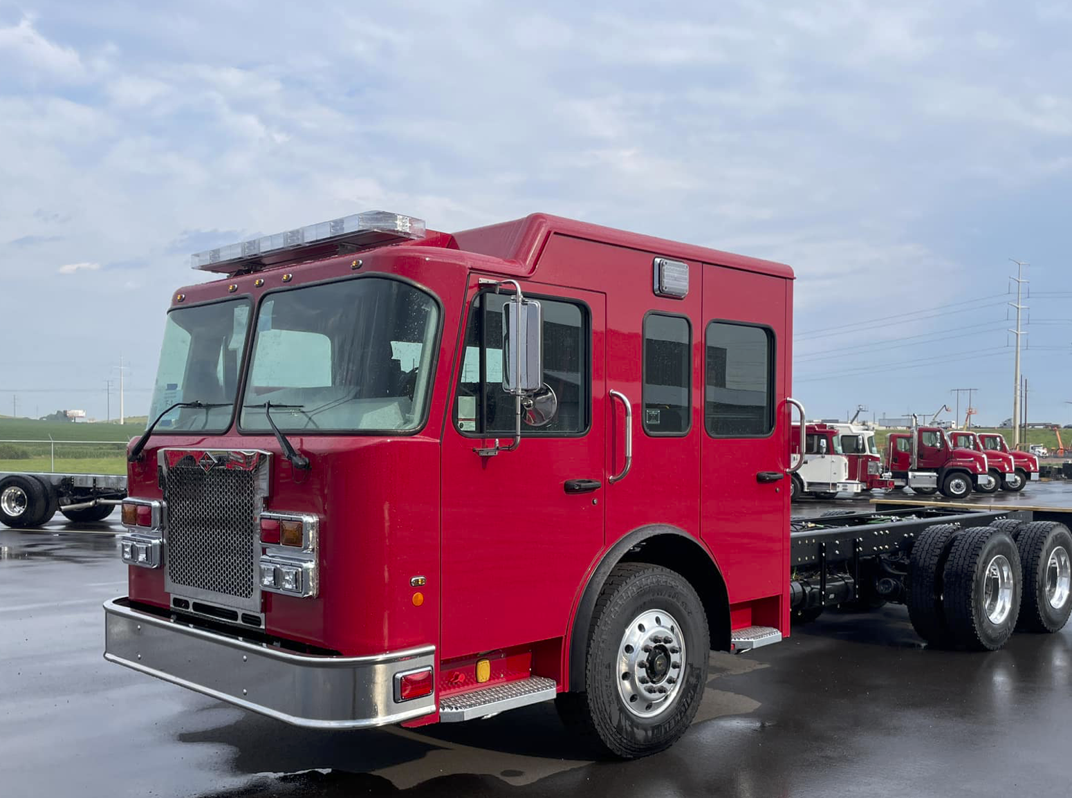 Red fire truck cabin on wet pavement with more trucks in the background.