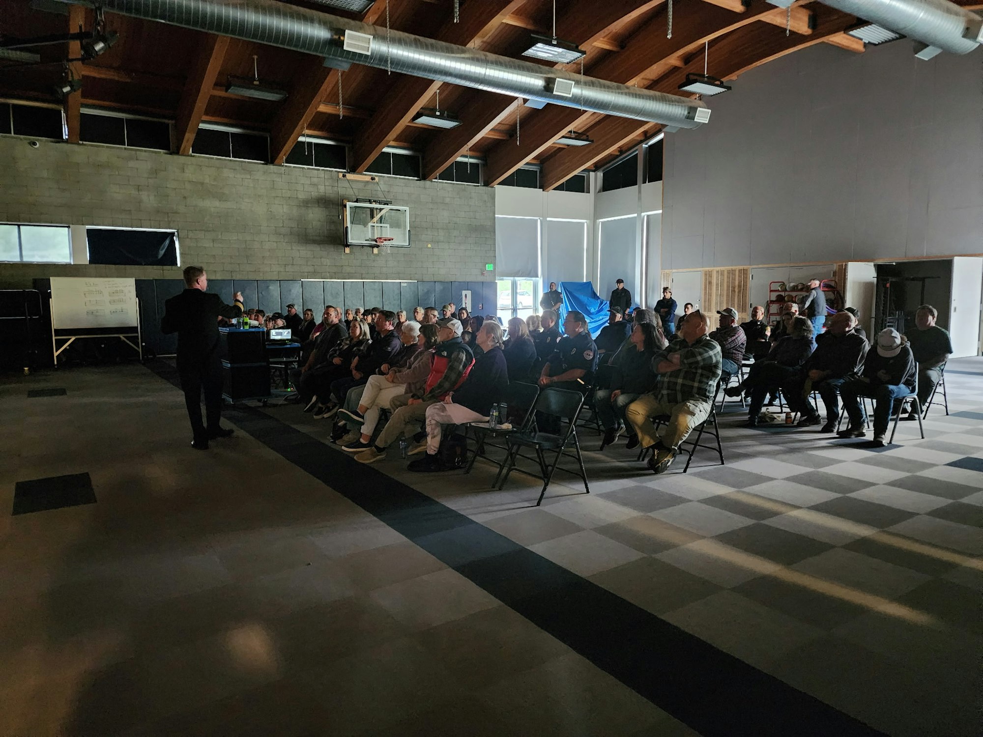 A presentation or meeting with a speaker addressing a seated audience in a large room.